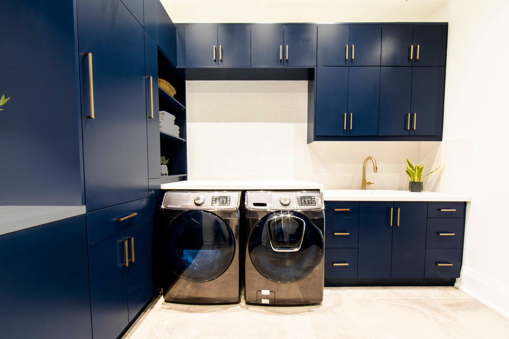 Mittelgroße Moderne Waschküche in L-Form mit flächenbündigen Schrankfronten, blauen Schränken, Mineralwerkstoff-Arbeitsplatte, weißer Wandfarbe, Travertin, Waschmaschine und Trockner nebeneinander, beigem Boden und weißer Arbeitsplatte in Toronto