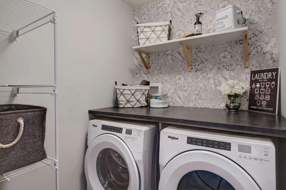 Modelo de cuarto de lavado lineal clásico renovado pequeño con encimera de laminado, paredes blancas, suelo vinílico, lavadora y secadora juntas, suelo gris y encimeras negras