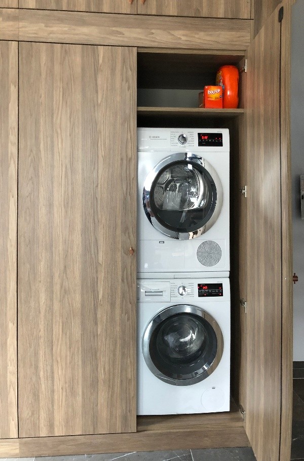 Imagen de armario lavadero lineal contemporáneo pequeño con armarios con paneles lisos, puertas de armario de madera oscura, paredes blancas, suelo de mármol, lavadora y secadora apiladas y suelo gris
