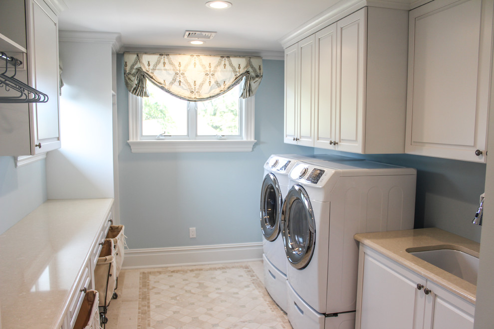 Immagine di una grande lavanderia multiuso stile shabby con lavello da incasso, ante bianche, pareti blu, pavimento con piastrelle in ceramica, lavatrice e asciugatrice affiancate e ante con bugna sagomata