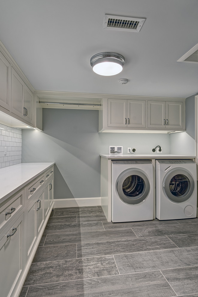 Klassisk inredning av en mellanstor l-formad tvättstuga enbart för tvätt, med skåp i shakerstil, vita skåp, bänkskiva i kvartsit, grå väggar, klinkergolv i porslin, en tvättmaskin och torktumlare bredvid varandra och brunt golv