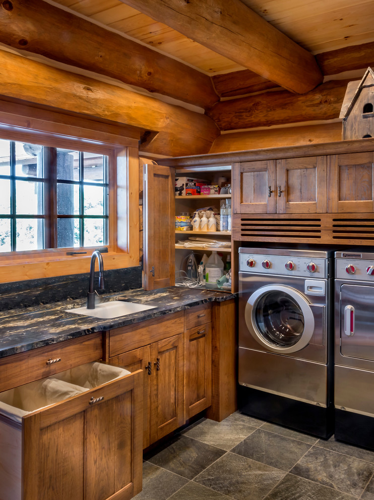Exempel på en stor rustik l-formad tvättstuga enbart för tvätt, med en undermonterad diskho, luckor med infälld panel, skåp i mellenmörkt trä, granitbänkskiva, skiffergolv och en tvättmaskin och torktumlare bredvid varandra