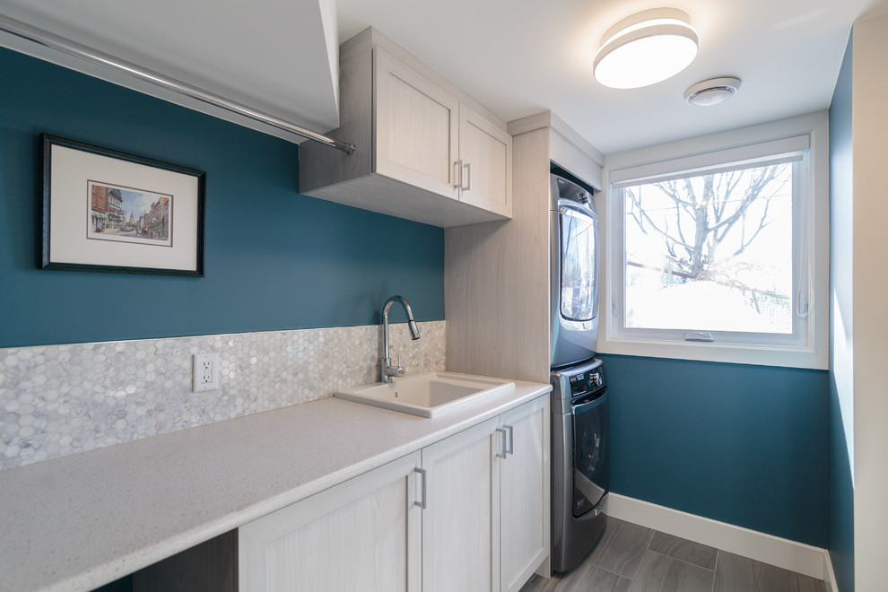 Einzeilige, Mittelgroße Klassische Waschküche mit Einbauwaschbecken, Schrankfronten im Shaker-Stil, weißen Schränken, blauer Wandfarbe, Porzellan-Bodenfliesen und Waschmaschine und Trockner gestapelt in Montreal
