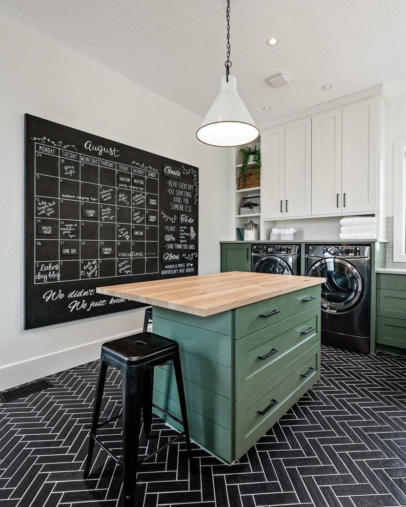ポートランドにあるカントリー風のおしゃれな家事室 (シェーカースタイル扉のキャビネット、緑のキャビネット、木材カウンター、白い壁、左右配置の洗濯機・乾燥機、黒い床) の写真