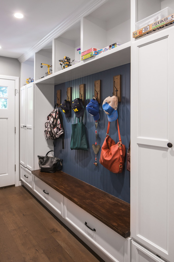 Modelo de cuarto de lavado de galera clásico renovado de tamaño medio con puertas de armario blancas, encimera de cuarzo compacto, paredes azules, suelo de madera en tonos medios, lavadora y secadora juntas y suelo marrón