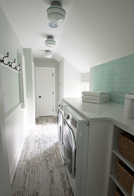 Bild på en liten lantlig linjär tvättstuga enbart för tvätt, med luckor med upphöjd panel, vita skåp, marmorbänkskiva, gröna väggar, klinkergolv i porslin och en tvättmaskin och torktumlare bredvid varandra
