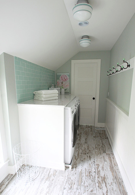 Foto på en liten lantlig linjär tvättstuga enbart för tvätt, med luckor med upphöjd panel, vita skåp, marmorbänkskiva, klinkergolv i porslin, en tvättmaskin och torktumlare bredvid varandra och grå väggar