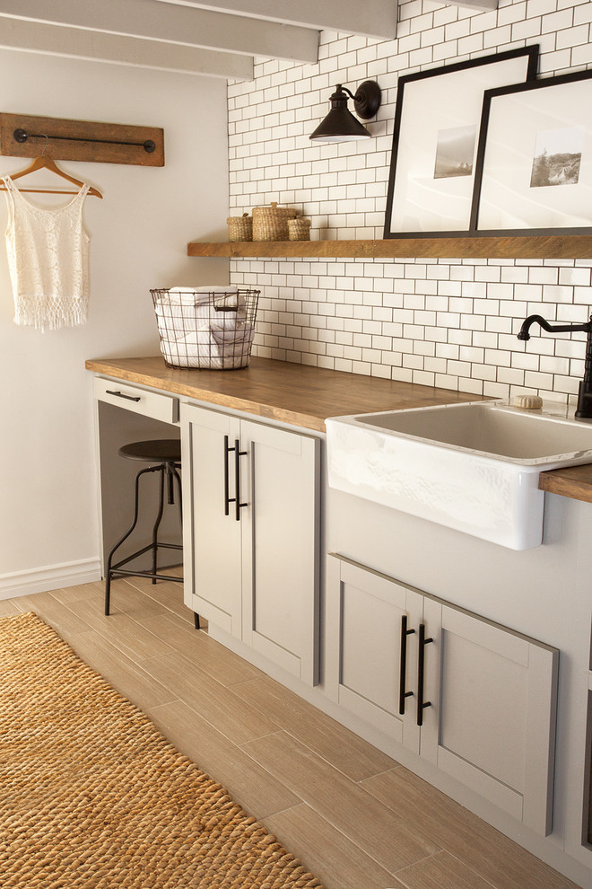 Dedicated laundry room - mid-sized farmhouse dedicated laundry room idea in Tampa with a farmhouse sink, shaker cabinets, gray cabinets, wood countertops, white walls, a side-by-side washer/dryer and brown countertops