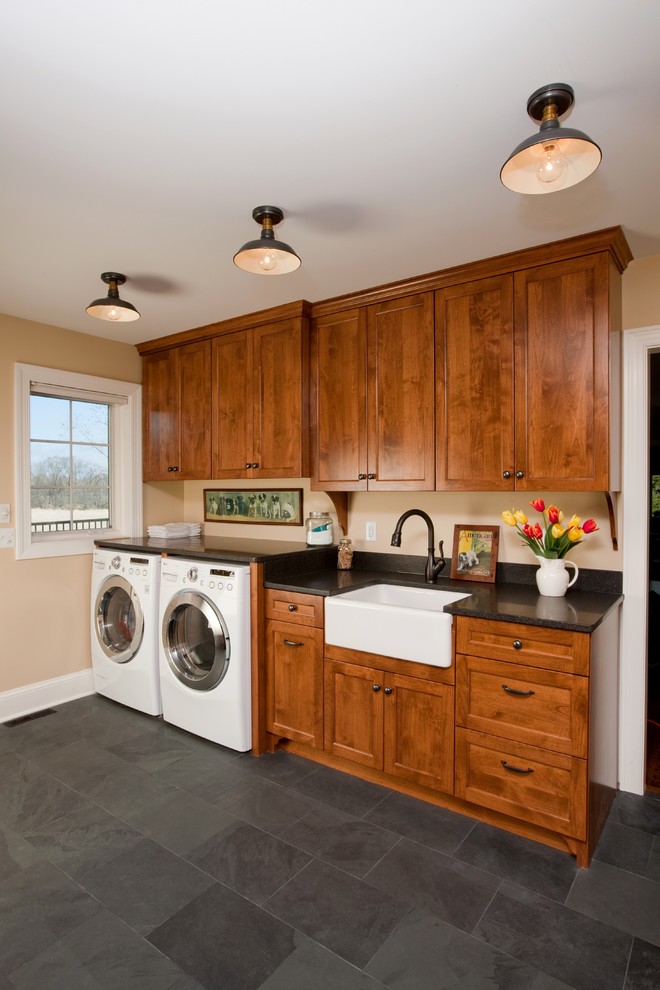 Inspiration for a medium sized country single-wall utility room in Minneapolis with a belfast sink, shaker cabinets, medium wood cabinets, granite worktops, beige walls, slate flooring and a side by side washer and dryer.