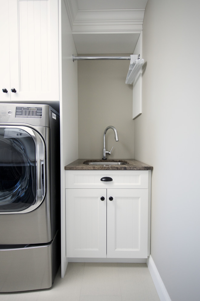 Exempel på en stor amerikansk parallell tvättstuga enbart för tvätt, med en undermonterad diskho, skåp i shakerstil, vita skåp, granitbänkskiva, grå väggar, klinkergolv i keramik och en tvättmaskin och torktumlare bredvid varandra