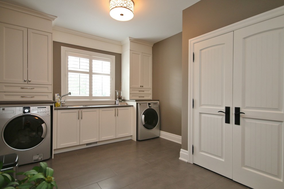 Modelo de lavadero clásico renovado de tamaño medio con puertas de armario blancas, encimera de laminado, paredes marrones y lavadora y secadora juntas