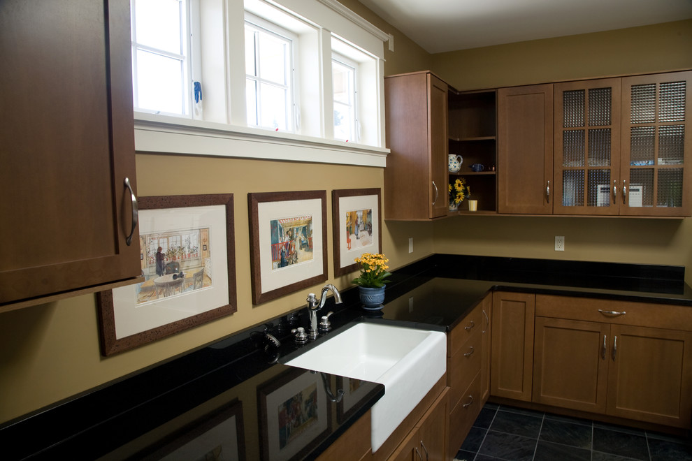 This is an example of a large traditional l-shaped separated utility room in Seattle with a belfast sink, shaker cabinets, medium wood cabinets, engineered stone countertops, beige walls, slate flooring, black floors and black worktops.