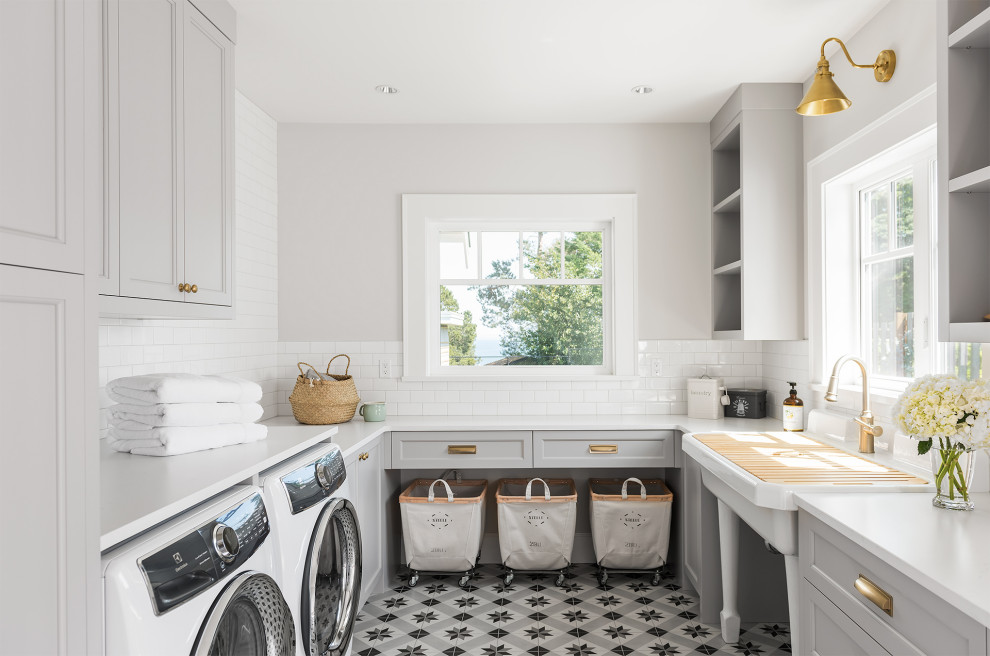 Inredning av en klassisk vita u-formad vitt tvättstuga enbart för tvätt, med en allbänk, luckor med infälld panel, grå skåp, grå väggar, en tvättmaskin och torktumlare bredvid varandra och flerfärgat golv