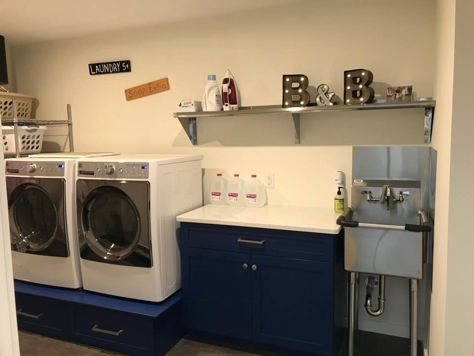 Immagine di una sala lavanderia minimalista di medie dimensioni con lavatoio, ante in stile shaker, ante blu, top in quarzo composito, pareti bianche, parquet scuro, lavatrice e asciugatrice affiancate, pavimento marrone e top bianco