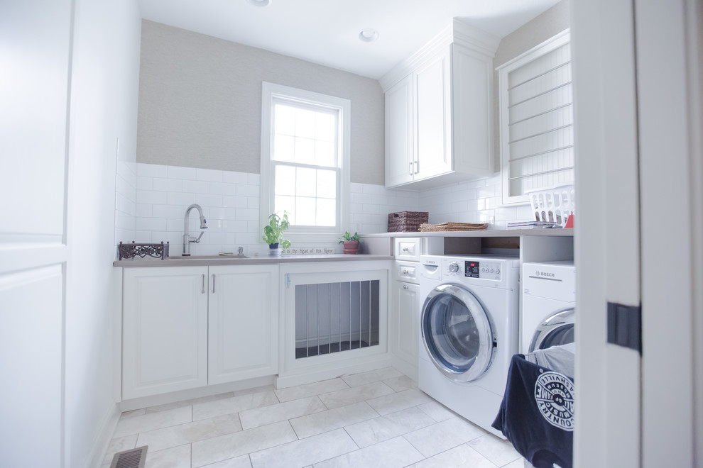 Immagine di una sala lavanderia american style di medie dimensioni con ante in stile shaker, ante bianche, pareti beige, pavimento in gres porcellanato, lavatrice e asciugatrice affiancate e pavimento bianco