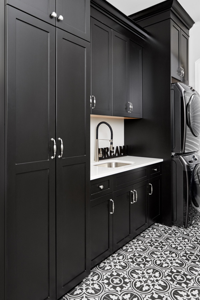 This is an example of a classic single-wall separated utility room in Toronto with a submerged sink, shaker cabinets, black cabinets, quartz worktops, white walls, porcelain flooring, a stacked washer and dryer, black floors and white worktops.