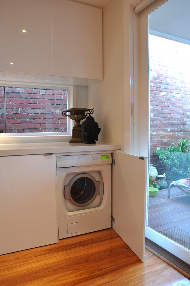 Foto di una lavanderia moderna con ante lisce, ante bianche, pareti bianche e parquet chiaro