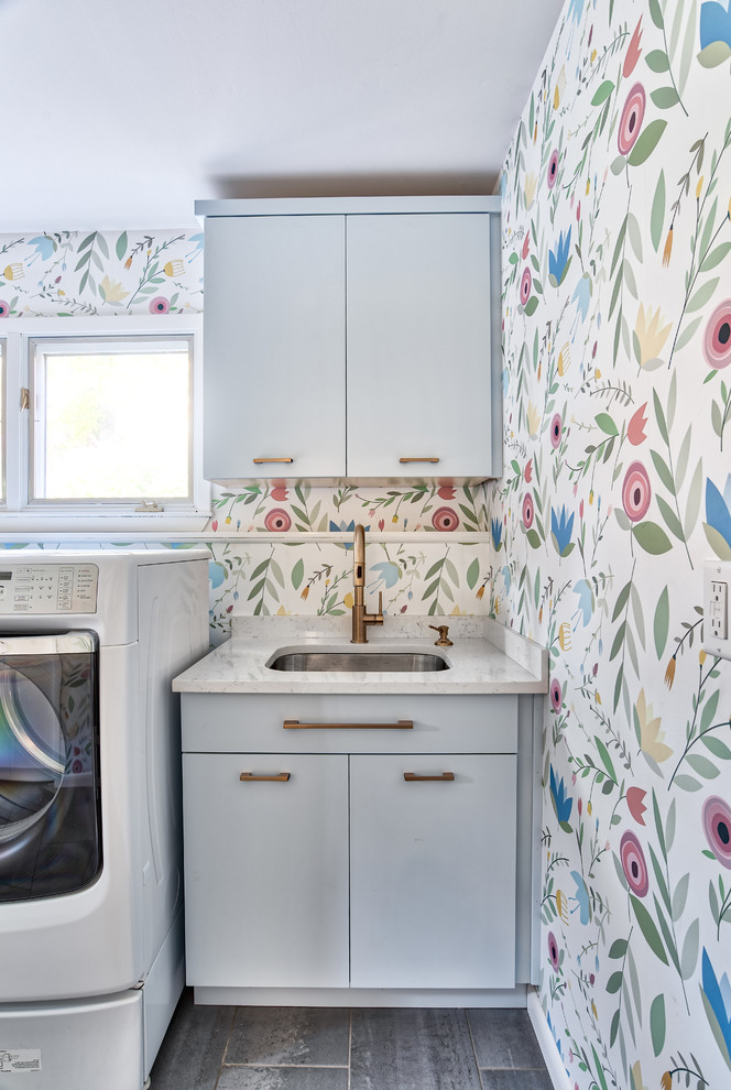 Idee per una grande lavanderia multiuso minimalista con lavello da incasso, ante lisce, ante blu, pareti multicolore, pavimento in gres porcellanato, lavatrice e asciugatrice affiancate, pavimento grigio e top bianco