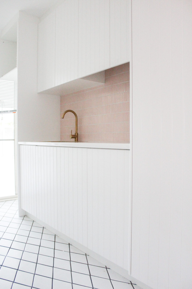 Medium sized modern single-wall separated utility room in Perth with a built-in sink, shaker cabinets, white cabinets, engineered stone countertops, pink splashback, mosaic tiled splashback, white walls, porcelain flooring, a stacked washer and dryer, white floors and white worktops.