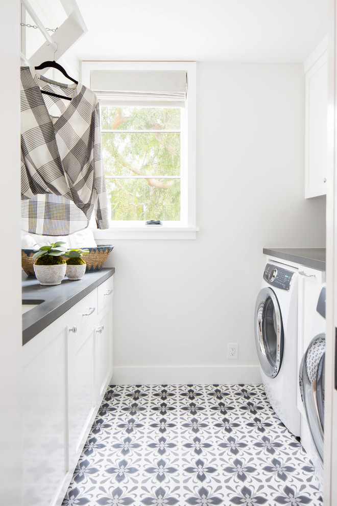 Immagine di una sala lavanderia costiera di medie dimensioni con lavello sottopiano, ante in stile shaker, ante bianche, pareti bianche, lavatrice e asciugatrice affiancate, top grigio e pavimento grigio