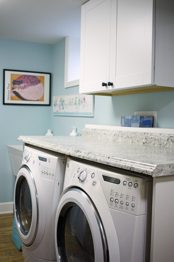 Idéer för att renovera en mellanstor vintage linjär tvättstuga enbart för tvätt, med en allbänk, luckor med infälld panel, vita skåp, granitbänkskiva, blå väggar, mellanmörkt trägolv och en tvättmaskin och torktumlare bredvid varandra