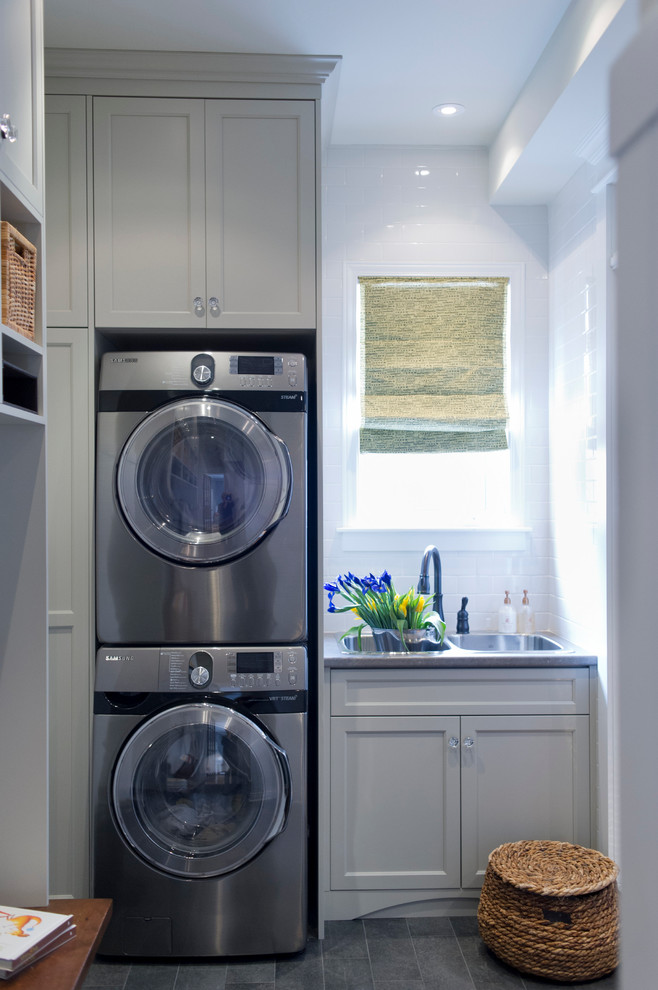 Utility room - small transitional single-wall ceramic tile utility room idea in Toronto with a drop-in sink, shaker cabinets, gray cabinets, laminate countertops, white walls and a stacked washer/dryer