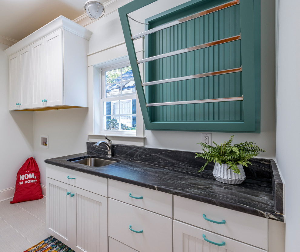 Inspiration for a medium sized traditional single-wall utility room in Raleigh with a submerged sink, recessed-panel cabinets, white cabinets, granite worktops, white walls, ceramic flooring, a side by side washer and dryer and black worktops.