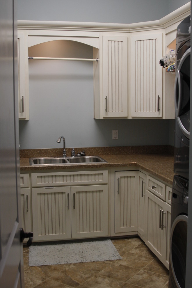 Inredning av en klassisk mellanstor l-formad tvättstuga enbart för tvätt, med en dubbel diskho, vita skåp, laminatbänkskiva, klinkergolv i keramik, en tvättpelare, luckor med infälld panel och grå väggar
