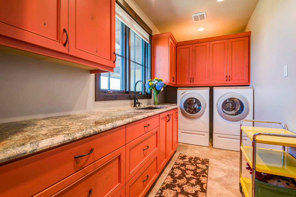 Große Rustikale Waschküche in L-Form mit Unterbauwaschbecken, Kassettenfronten, orangefarbenen Schränken, Granit-Arbeitsplatte, beiger Wandfarbe, Keramikboden, Waschmaschine und Trockner nebeneinander, beigem Boden und bunter Arbeitsplatte in Denver