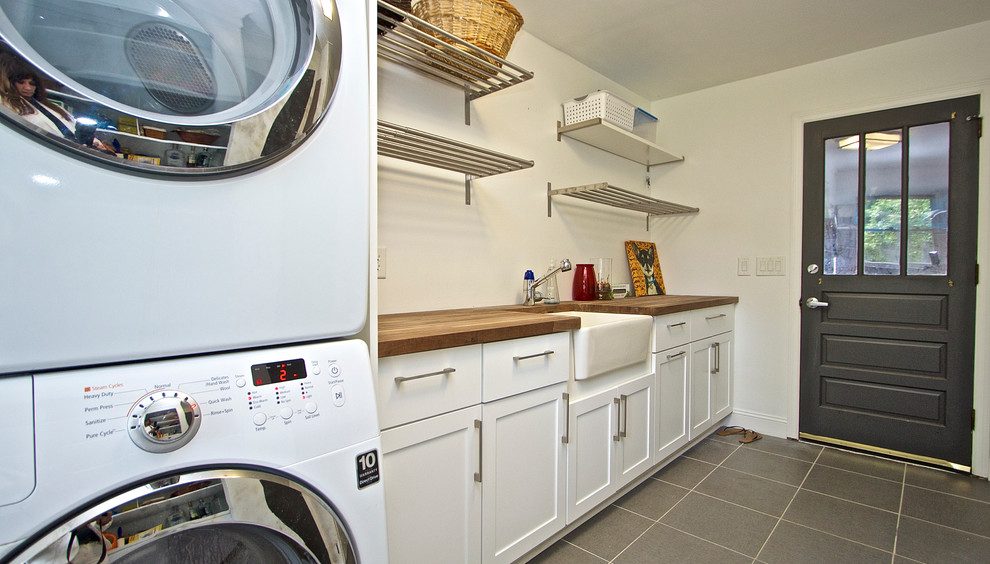 Dedicated laundry room - mid-sized coastal u-shaped porcelain tile dedicated laundry room idea in Charleston with a farmhouse sink, shaker cabinets, white cabinets, wood countertops, white walls and a stacked washer/dryer