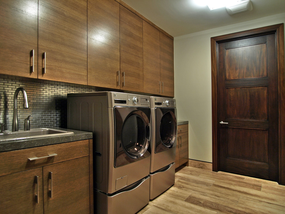 Modelo de lavadero actual con fregadero encastrado, armarios con paneles lisos, puertas de armario de madera en tonos medios, lavadora y secadora juntas y suelo marrón