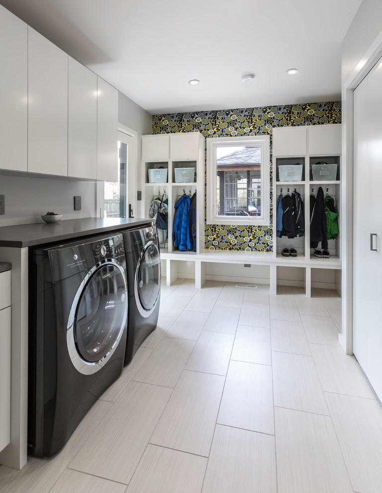 Inspiration for a large contemporary single-wall utility room in Milwaukee with flat-panel cabinets, white cabinets, quartz worktops, grey walls, laminate floors, a side by side washer and dryer, white floors, grey worktops and a feature wall.
