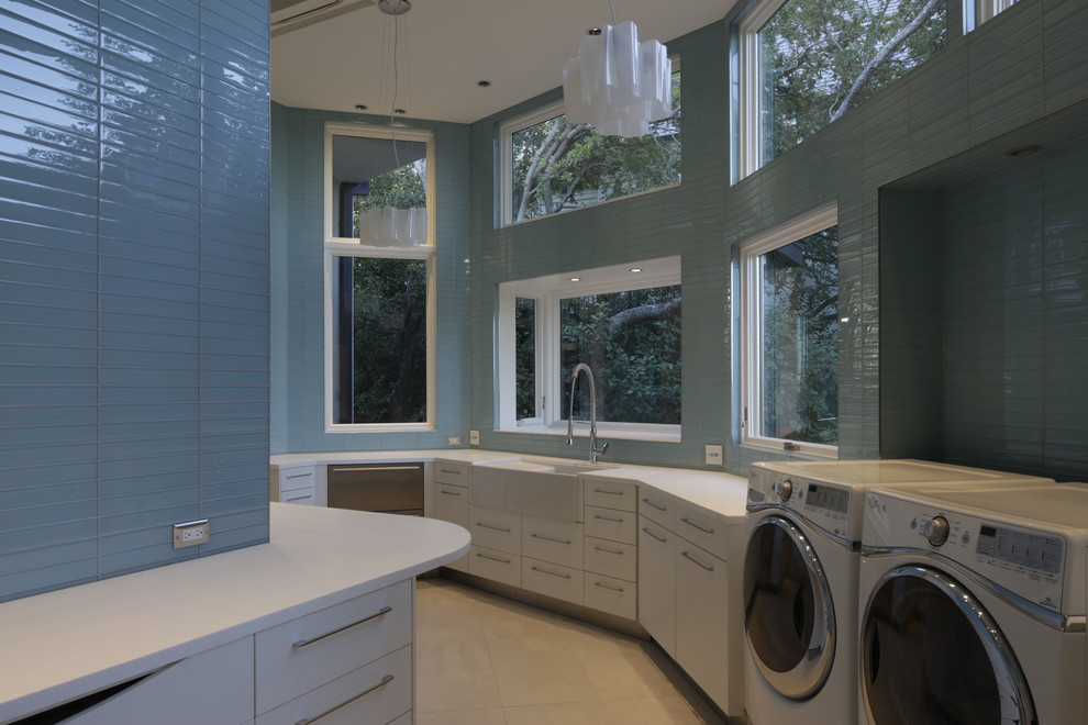Inredning av en stor u-formad tvättstuga enbart för tvätt, med en rustik diskho, släta luckor, vita skåp, bänkskiva i koppar, blå väggar, travertin golv och en tvättmaskin och torktumlare bredvid varandra