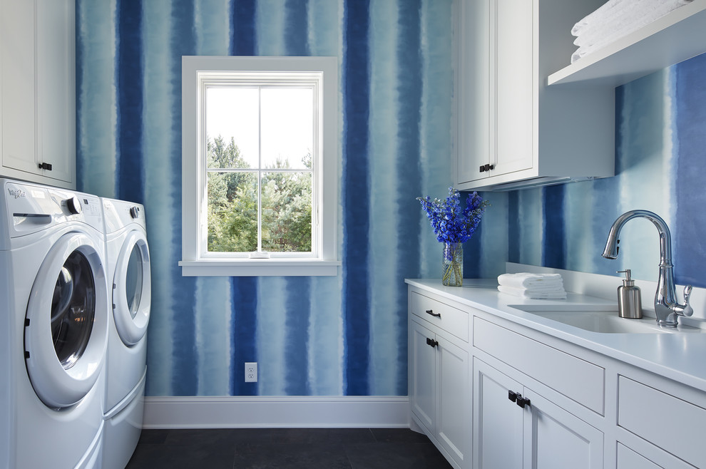 Immagine di una sala lavanderia country di medie dimensioni con ante bianche, pavimento in ardesia, lavatrice e asciugatrice affiancate, lavello sottopiano, top in quarzo composito, top bianco, ante con riquadro incassato e pareti blu