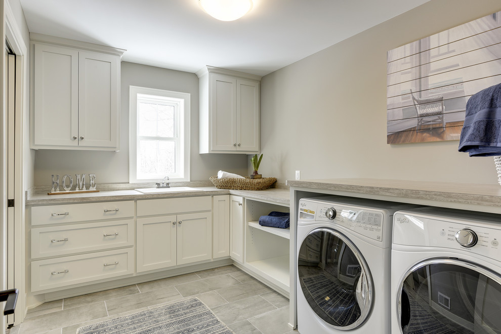 Idéer för en stor klassisk grå l-formad tvättstuga enbart för tvätt, med en nedsänkt diskho, skåp i shakerstil, vita skåp, laminatbänkskiva, grå väggar, klinkergolv i porslin, en tvättmaskin och torktumlare bredvid varandra och grått golv