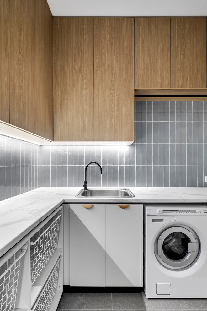 Idéer för en modern vita l-formad tvättstuga enbart för tvätt, med en nedsänkt diskho, släta luckor, vita skåp, grå väggar, en tvättmaskin och torktumlare bredvid varandra och grått golv