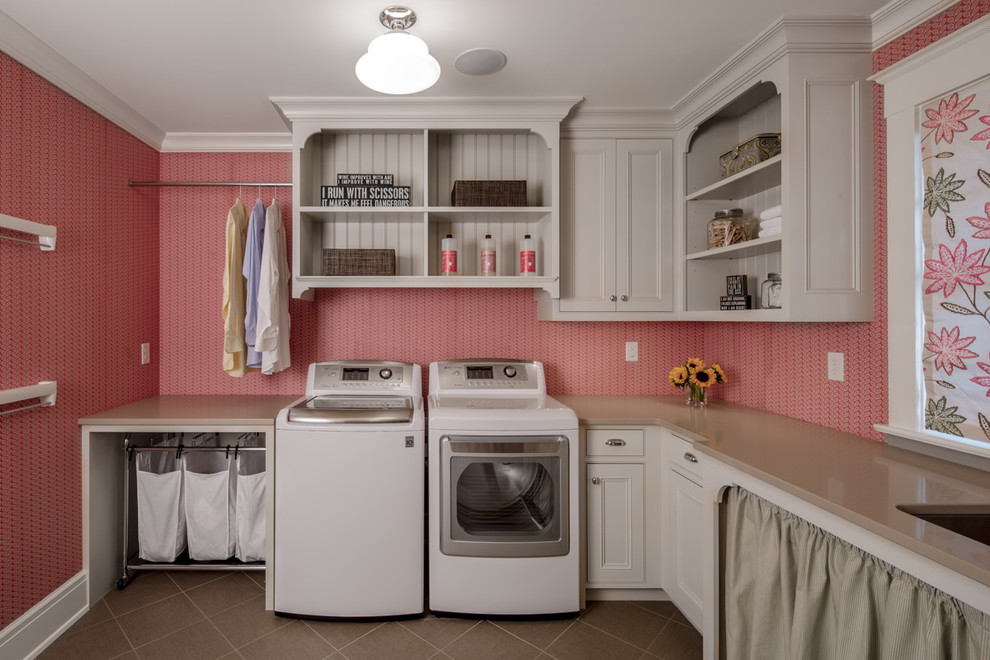 Diseño de cuarto de lavado en L tradicional con fregadero bajoencimera, puertas de armario beige, paredes rosas, lavadora y secadora juntas y armarios con rebordes decorativos