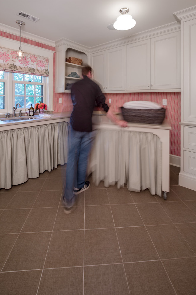 Inredning av en klassisk tvättstuga enbart för tvätt, med en undermonterad diskho, luckor med infälld panel, beige skåp, rosa väggar och en tvättmaskin och torktumlare bredvid varandra
