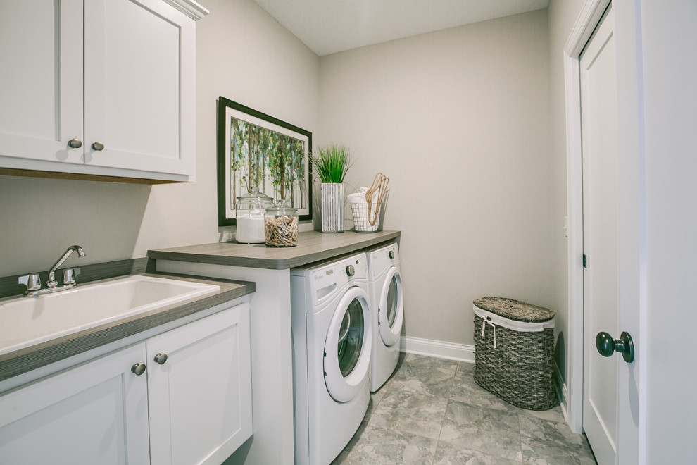 Exempel på en mellanstor klassisk linjär tvättstuga enbart för tvätt, med en nedsänkt diskho, luckor med profilerade fronter, vita skåp, laminatbänkskiva, grå väggar, vinylgolv, en tvättmaskin och torktumlare bredvid varandra och flerfärgat golv