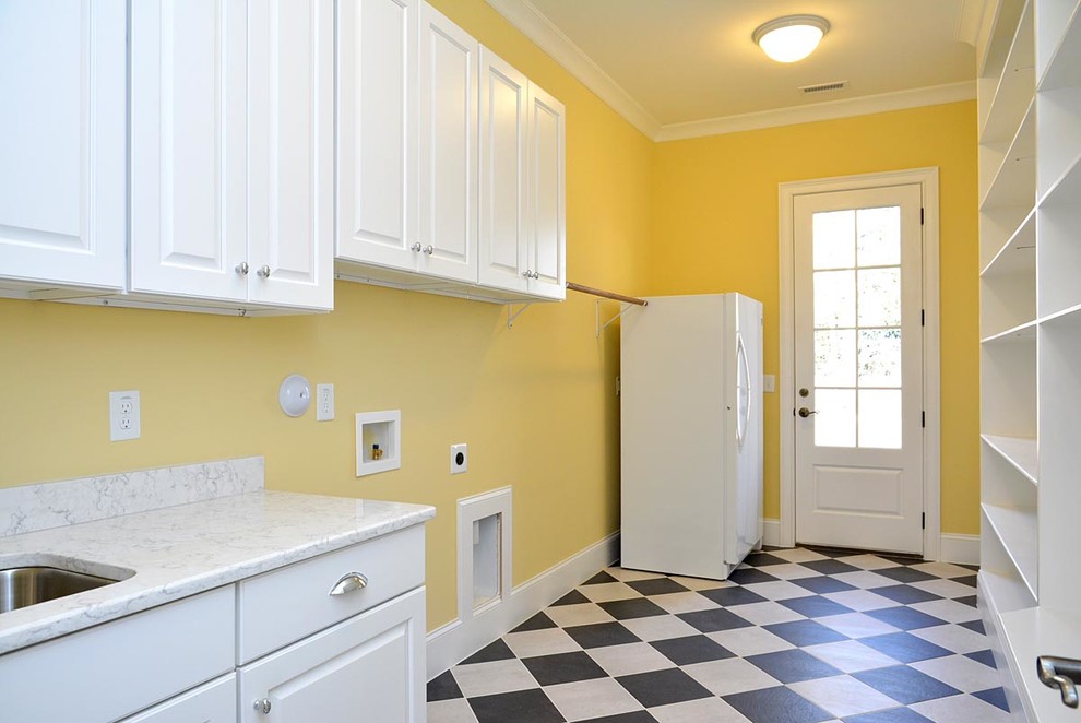 Bild på ett mycket stort parallellt grovkök, med en undermonterad diskho, luckor med upphöjd panel, vita skåp, marmorbänkskiva, gula väggar, klinkergolv i keramik och en tvättmaskin och torktumlare bredvid varandra