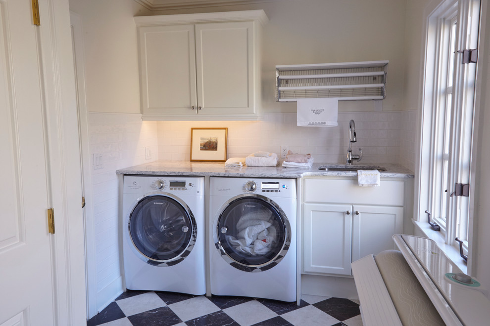Exempel på en mellanstor klassisk grå linjär grått tvättstuga enbart för tvätt, med en undermonterad diskho, skåp i shakerstil, vita skåp, granitbänkskiva, vita väggar, en tvättmaskin och torktumlare bredvid varandra och flerfärgat golv