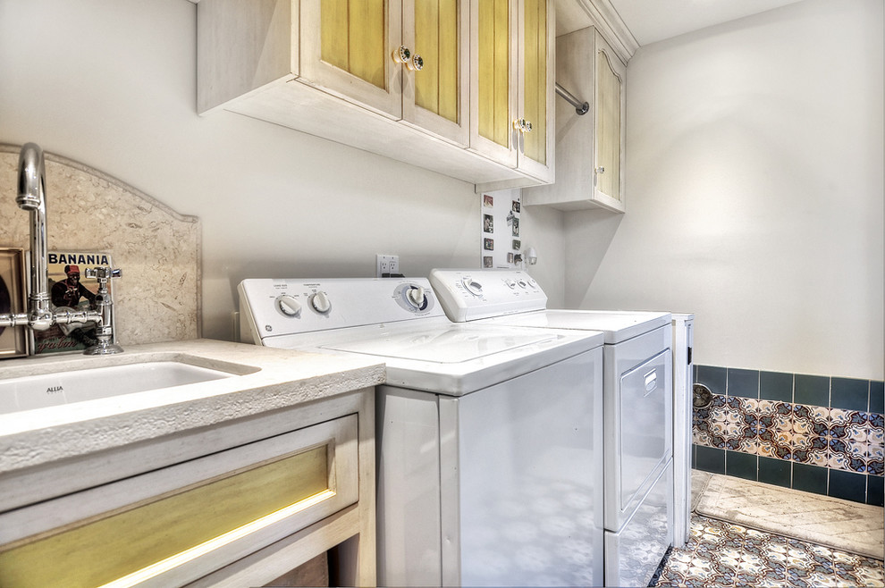 Foto di una lavanderia mediterranea di medie dimensioni con lavello da incasso, ante con bugna sagomata, ante gialle, top in granito, pareti bianche, pavimento in terracotta e lavatrice e asciugatrice affiancate