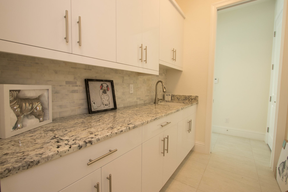 Einzeilige, Mittelgroße Klassische Waschküche mit Unterbauwaschbecken, flächenbündigen Schrankfronten, weißen Schränken, Granit-Arbeitsplatte, grauer Wandfarbe, Keramikboden und Waschmaschine und Trockner gestapelt in Miami