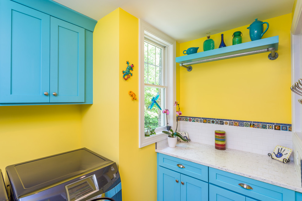 Immagine di una sala lavanderia tradizionale con ante in stile shaker, ante blu, pareti gialle, lavatrice e asciugatrice affiancate e top beige