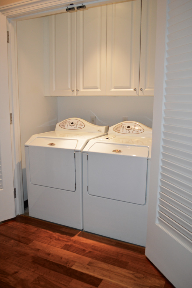 Idee per un piccolo ripostiglio-lavanderia tradizionale con ante con bugna sagomata, ante bianche, pareti bianche, pavimento in legno massello medio e lavatrice e asciugatrice affiancate