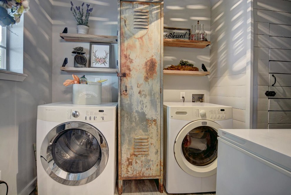 Exempel på en liten lantlig linjär tvättstuga enbart för tvätt, med skåp i slitet trä, grå väggar, mellanmörkt trägolv, en tvättmaskin och torktumlare bredvid varandra och grått golv