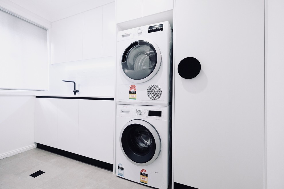 Medium sized modern galley separated utility room in Sydney with a built-in sink, white cabinets, engineered stone countertops, white walls, ceramic flooring, a stacked washer and dryer, grey floors and white worktops.