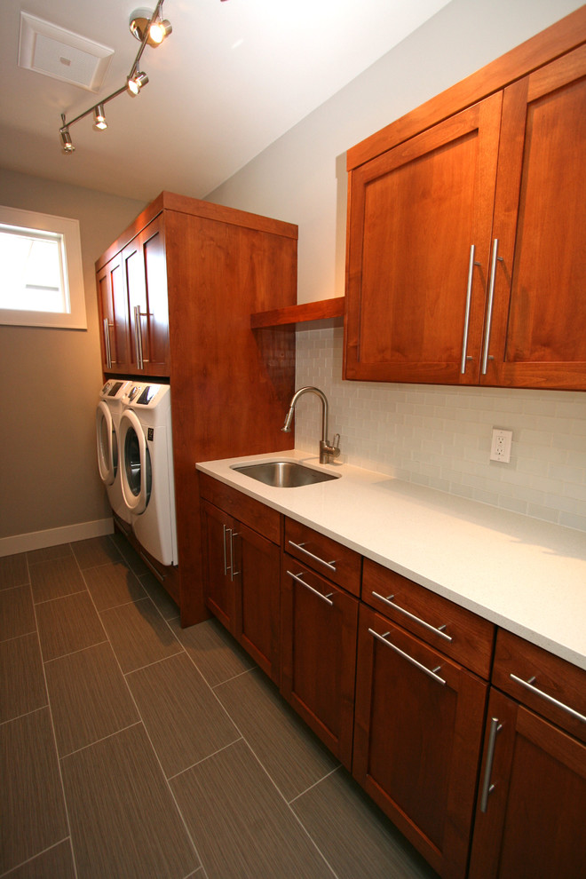 Example of a mid-sized trendy galley porcelain tile dedicated laundry room design in Seattle with an undermount sink, shaker cabinets, medium tone wood cabinets, quartz countertops, gray walls and a side-by-side washer/dryer