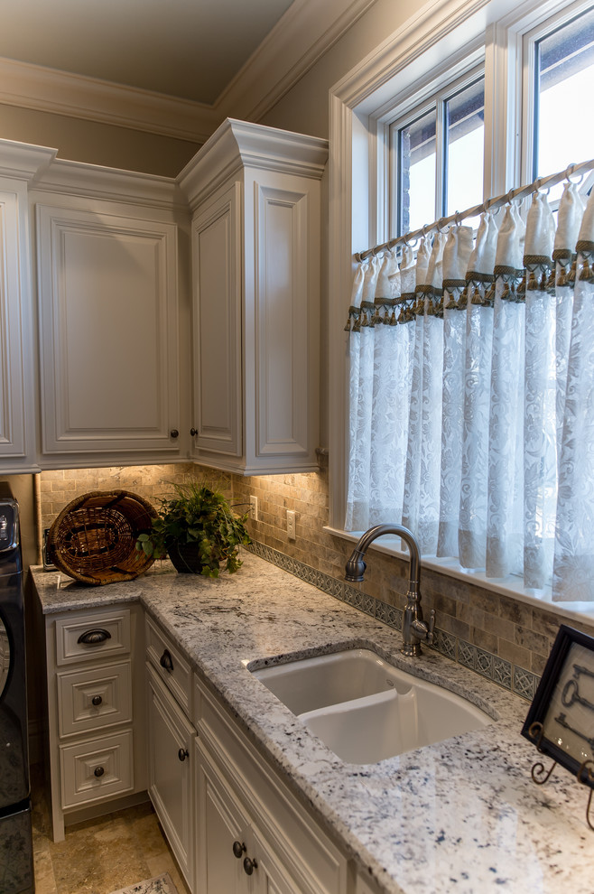 Inspiration for a large classic u-shaped separated utility room in Oklahoma City with a submerged sink, raised-panel cabinets, white cabinets, granite worktops, beige walls, travertine flooring, a side by side washer and dryer and beige floors.