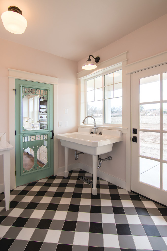 Photo of a small farmhouse u-shaped utility room in Seattle with a belfast sink, pink walls, ceramic flooring, a side by side washer and dryer and black floors.